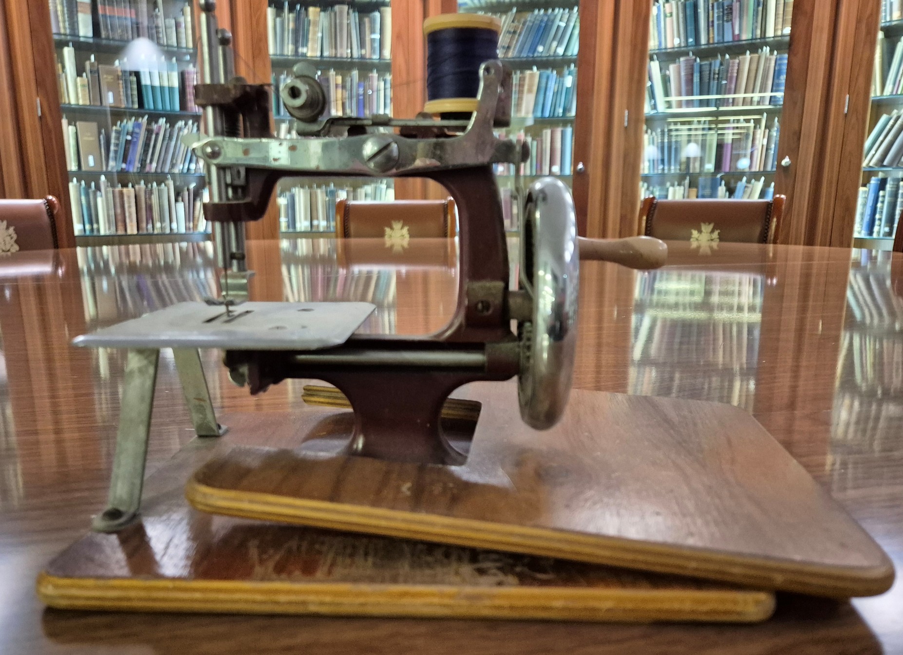 Colour photo of a small wooden and metal sewing machine with a hand crank. 