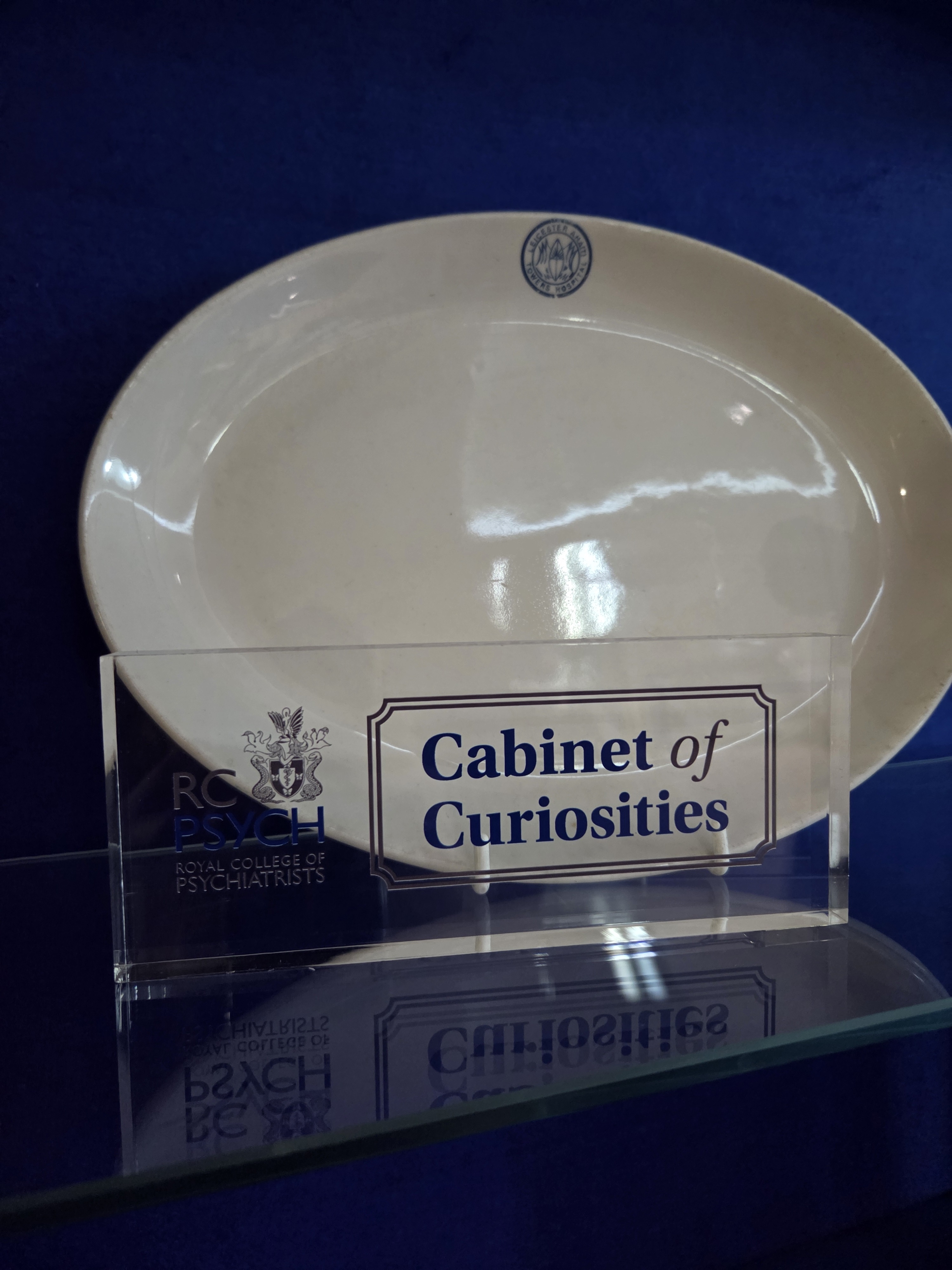 Photograph of a plain oval plate with a small monogram, inside the RCPsych Cabinet of Curiosities