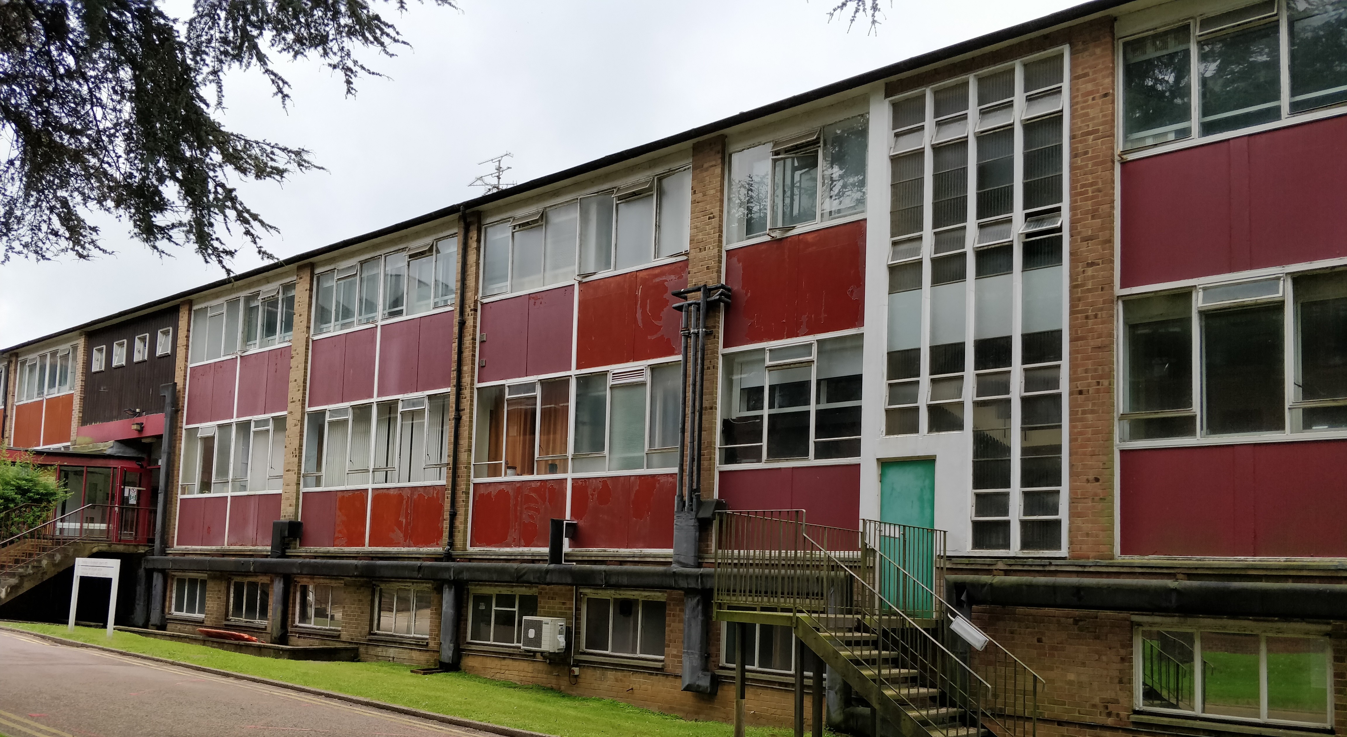 Three storey, red brick building with a flat roof that takes up the whole frame, with red cladding.