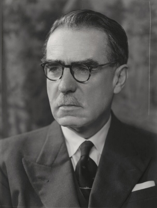 Black and white photo of a middle-aged white man wearing a suit with a mustache and glasses.