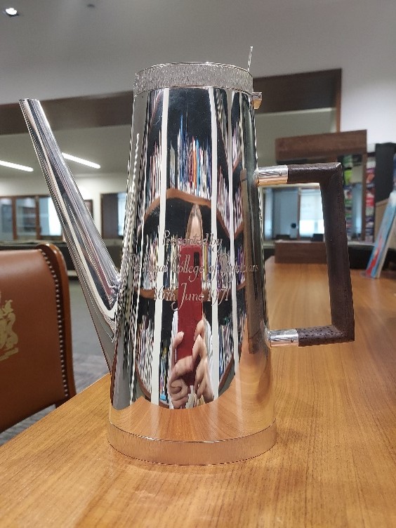 Silver coffee pot with engraved writing and a dark brown handle.