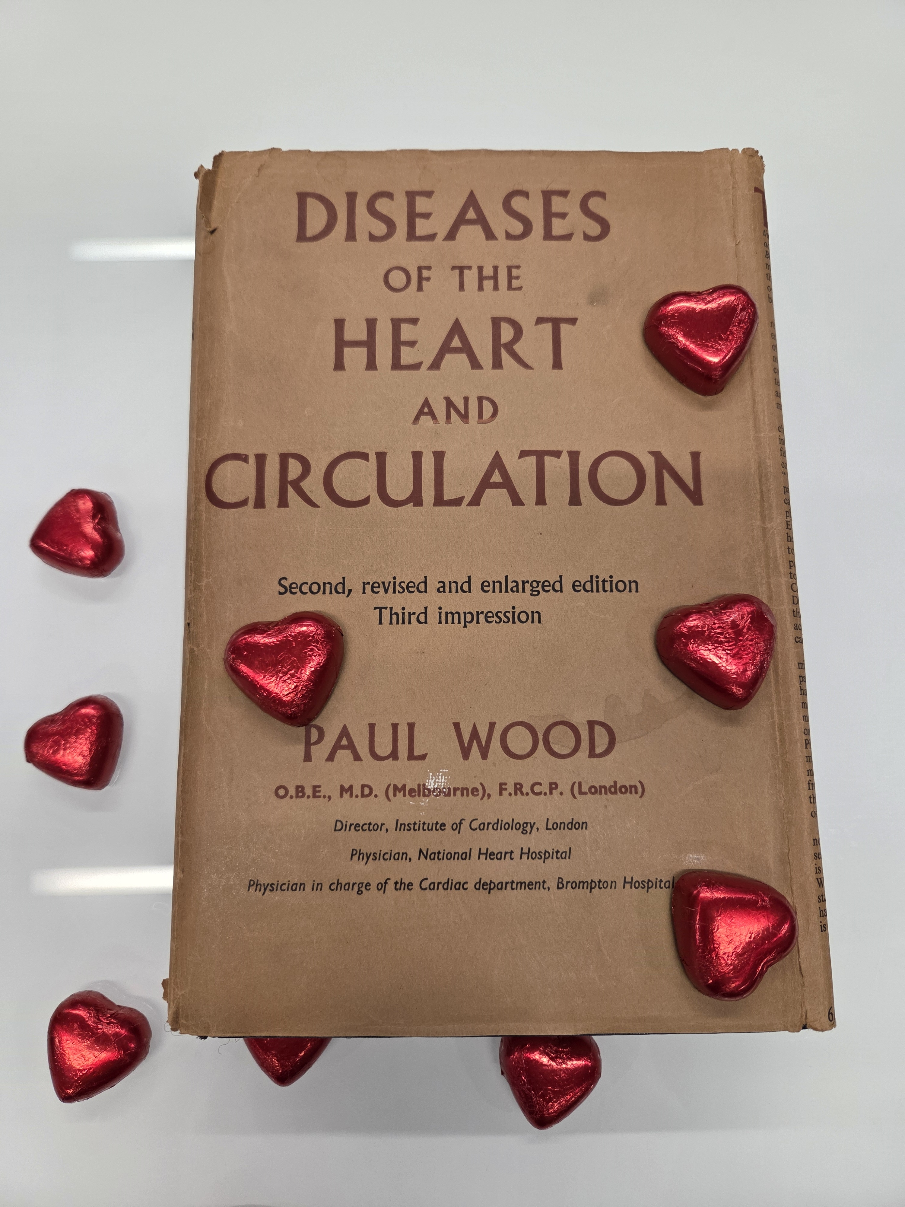 Colour photo of an old book: Diseases of the heart and circulation Paul Wood. There are foil wrapped red hearts scattered over the books and table.