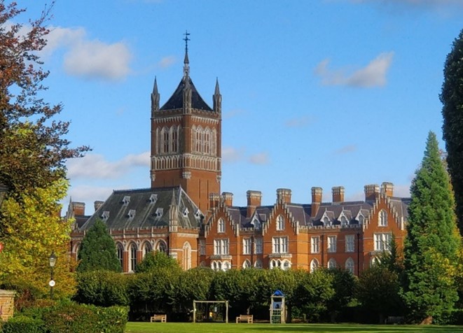 Fancy Victorian building in pale brick with ornate tower, surrounded by green lawn and trees.