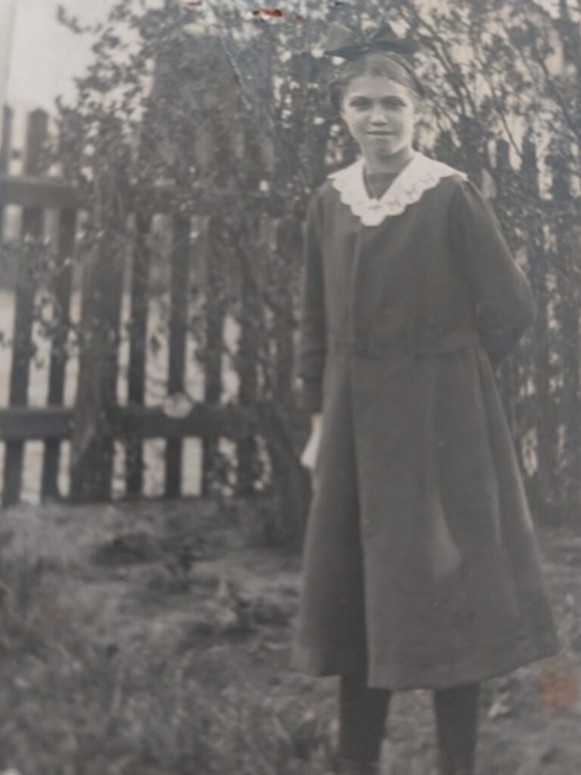 Black and white photo of a white girl around 12 standing in a garden.