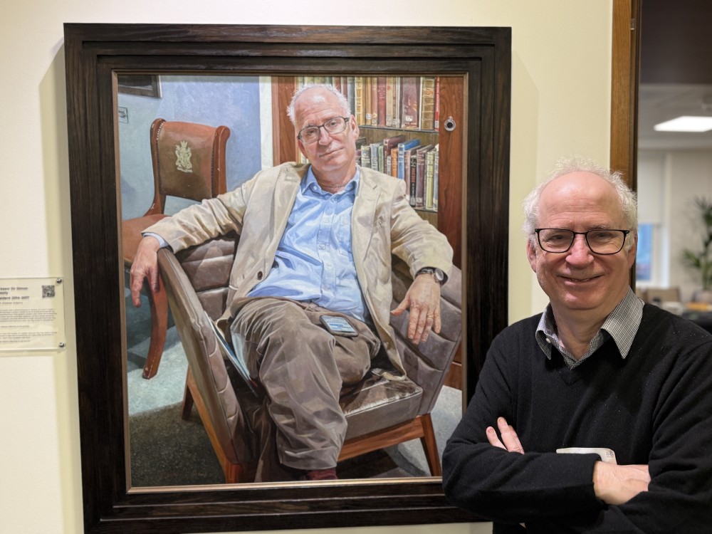 Professor Sir Simon Wessely standing next to his portrait