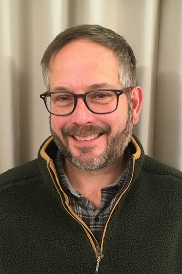 White man with salt and pepper hair and beard, smiling with glasses.